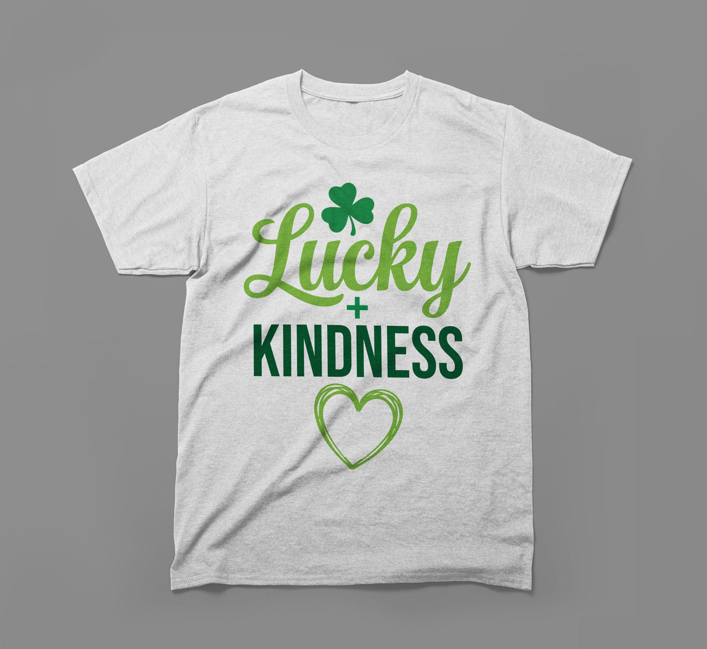 white t-shirt with green 'lucky + kindness' text, shamrock, and heart graphic on gray background.