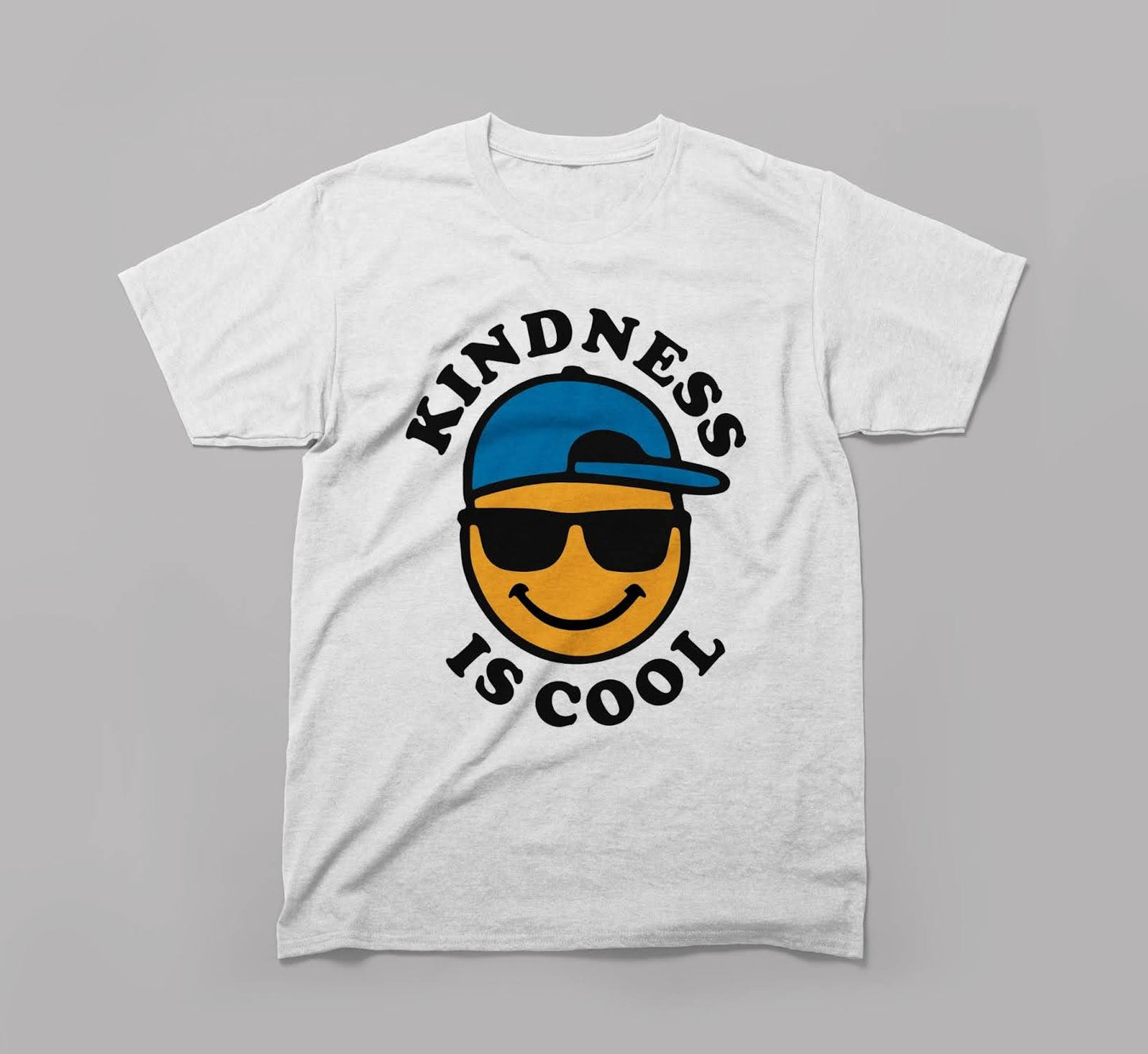 white t-shirt with 'kindness is cool' text and smiling emoji in sunglasses and blue cap.