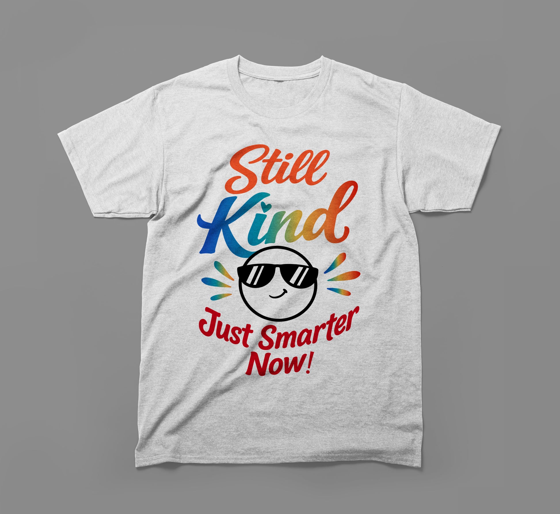 Grey t-shirt with rainbow text 'Still Kind Just Smarter Now' and smiley face in sunglasses.